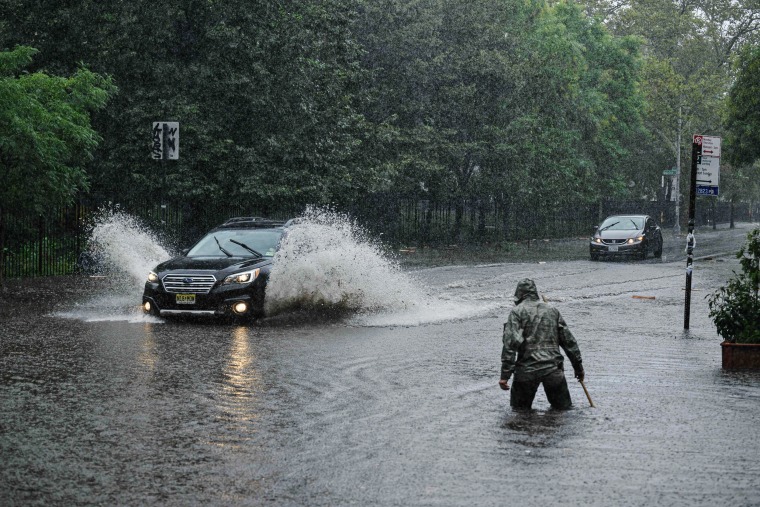 A man clears debris from a drain as a car make its way through floodwaters in Brooklyn, N.Y., on Sept. 29, 2023. 