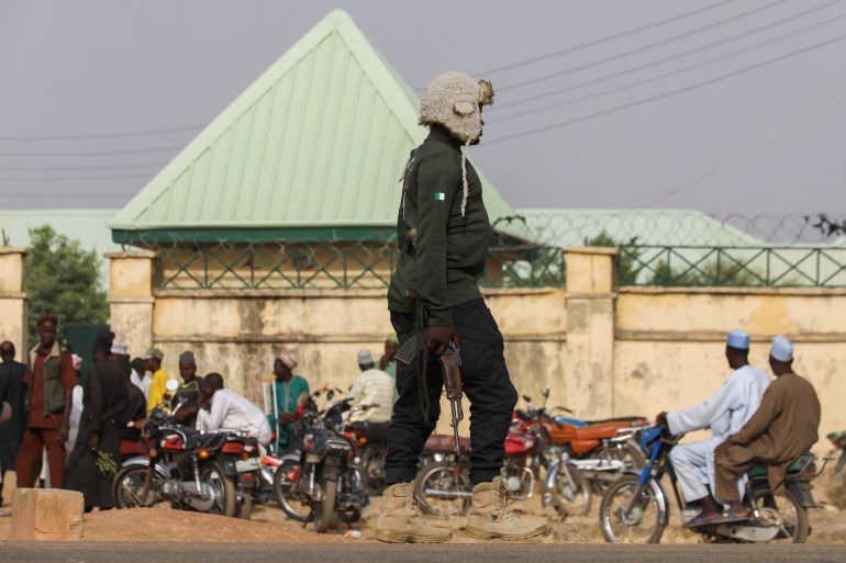 A security official walks near families of a kidnapped children in Nigeria